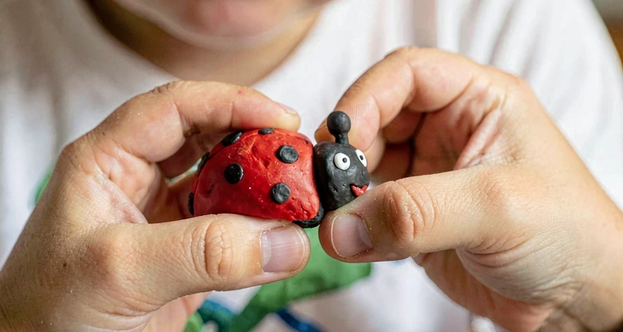 mãos de criança modelando escultura de joaninha com massinha colorida