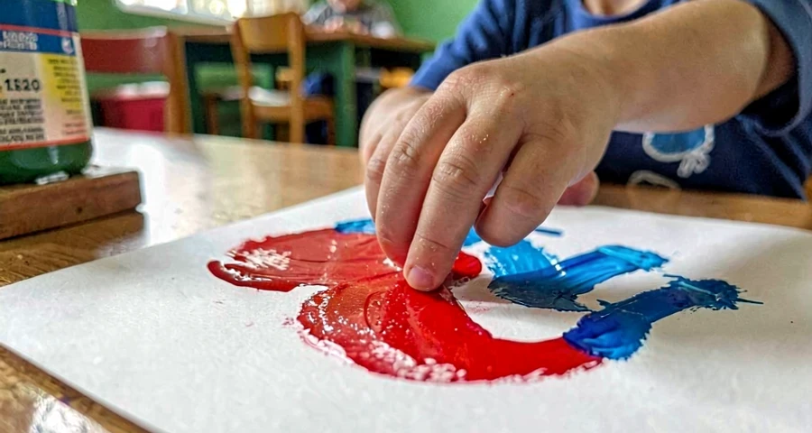 Marcas gráficas de bebê: detalhe de mão pequena deixando rastros coloridos em papel durante exploração sensorial com tinta